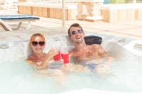 couple with drinks in sunshine outside in a hot tub